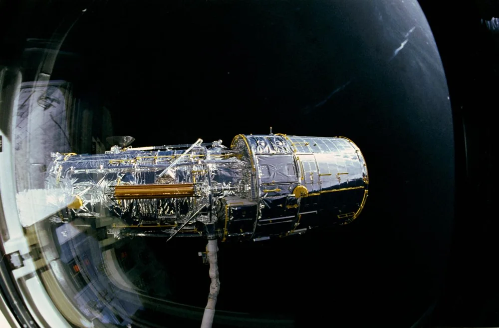 Hubble maintenu par le bras robotique de Discovery avant son déploiement en avril 1990. — Photographie